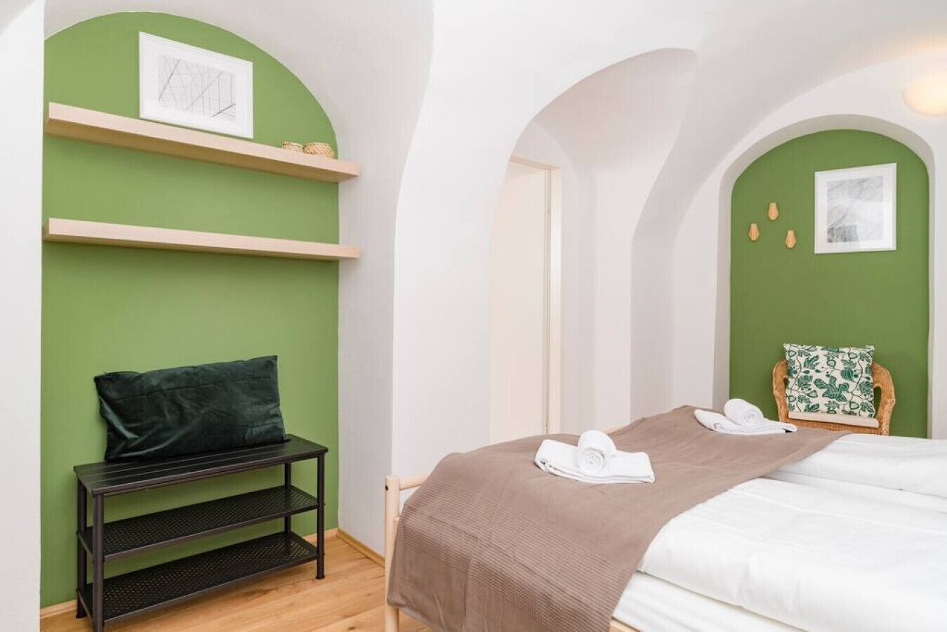 A hotel room with a bed, a small table, a chair, and a shelf with a pillow.
