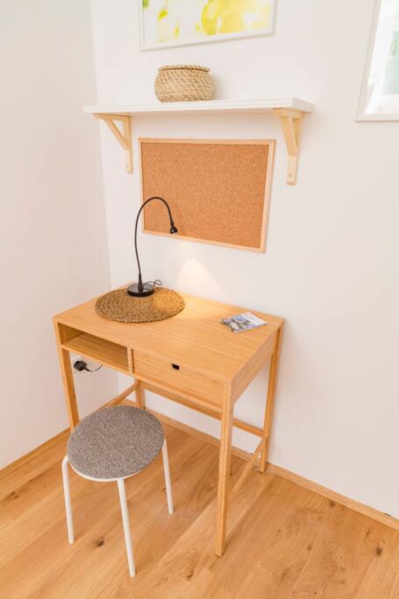 Un escritorio de madera con un corcho, una cesta tejida y una lámpara.