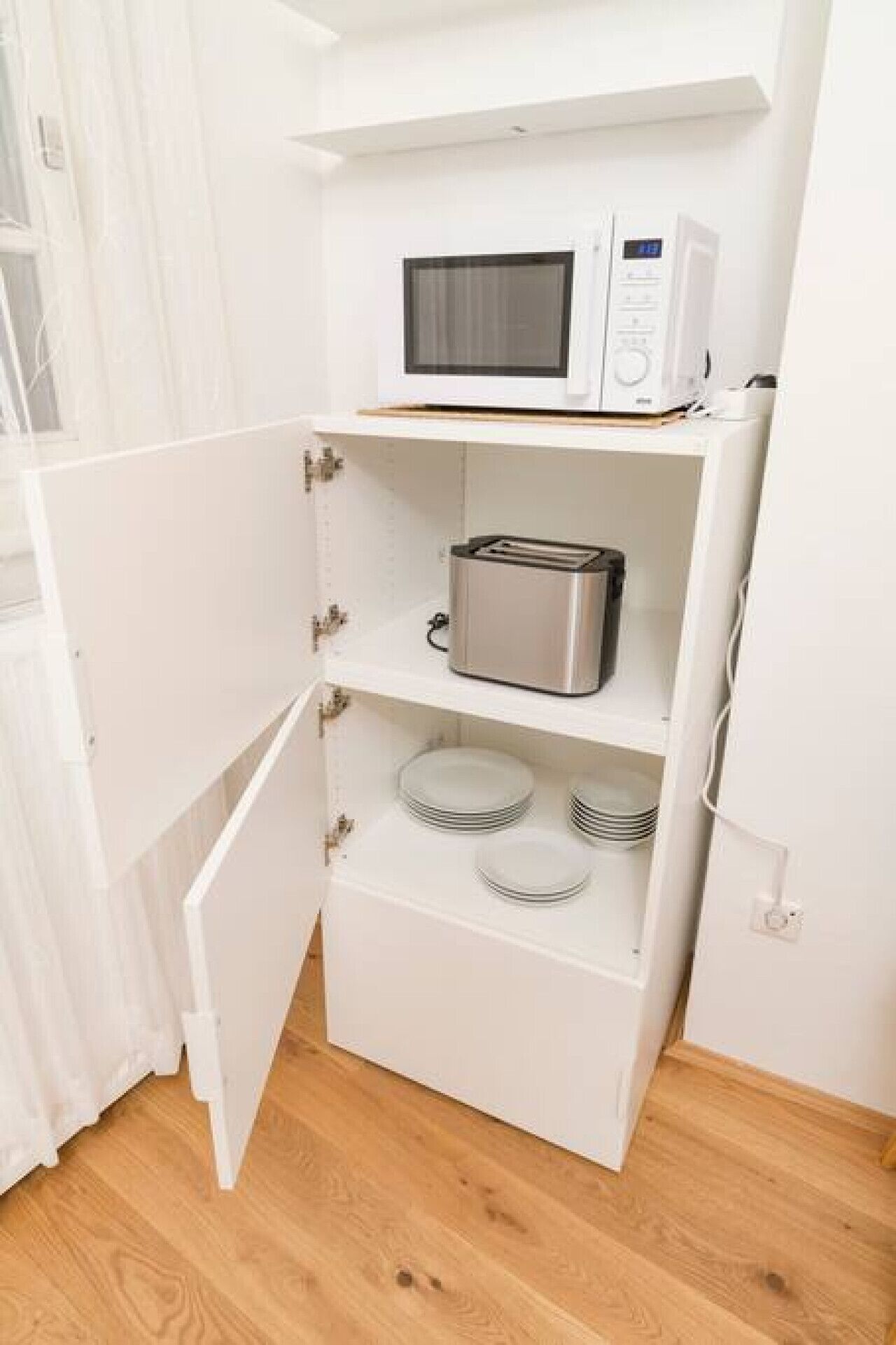 A compact kitchen with a microwave, toaster, and stacked plates on shelves.