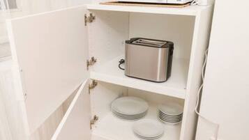 A compact kitchen with a microwave, toaster, and stacked plates on shelves.