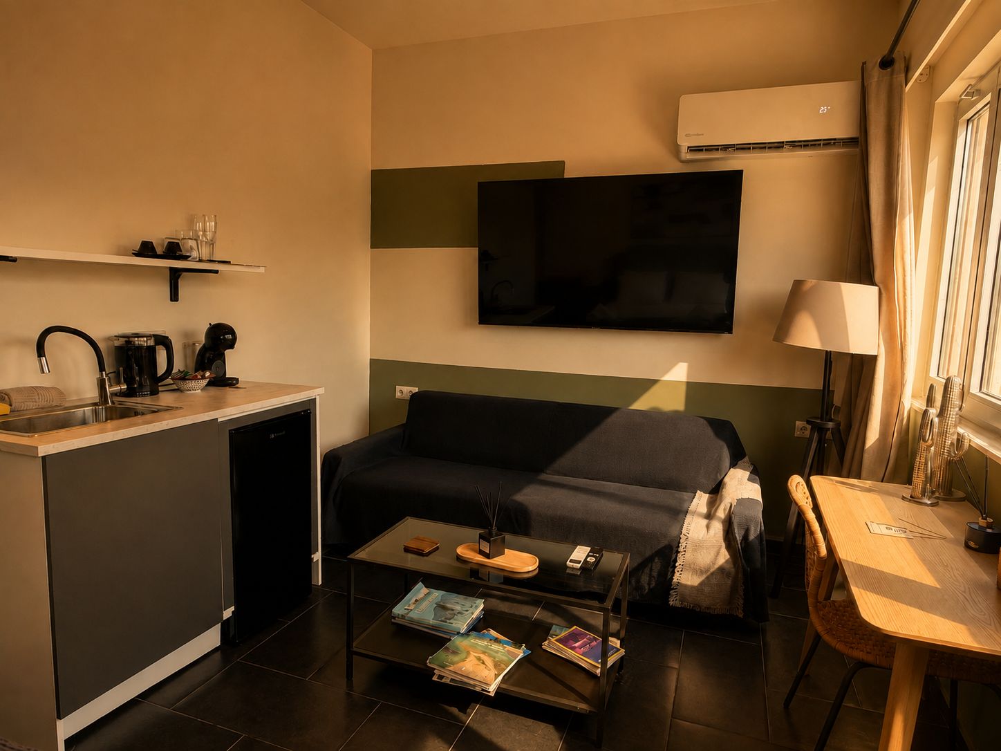 Habitación de hotel pequeña con kitchenette, un sofá, una mesa de centro y un televisor montado en la pared.