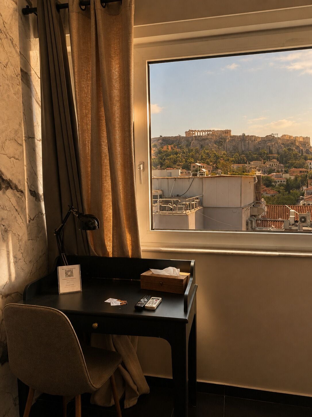 Una habitación con escritorio, silla y ventana con vista a un paisaje urbano con edificios históricos.