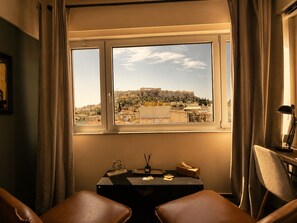 A room with a view of a historical cityscape through a window, a table with a lamp, and two chairs. - Elite Ermou Suites (Athens)