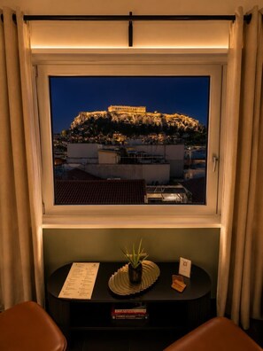 A room with a view of a historic building at night, a small table with a menu, and a plant. - Elite Ermou Suites (Athens)