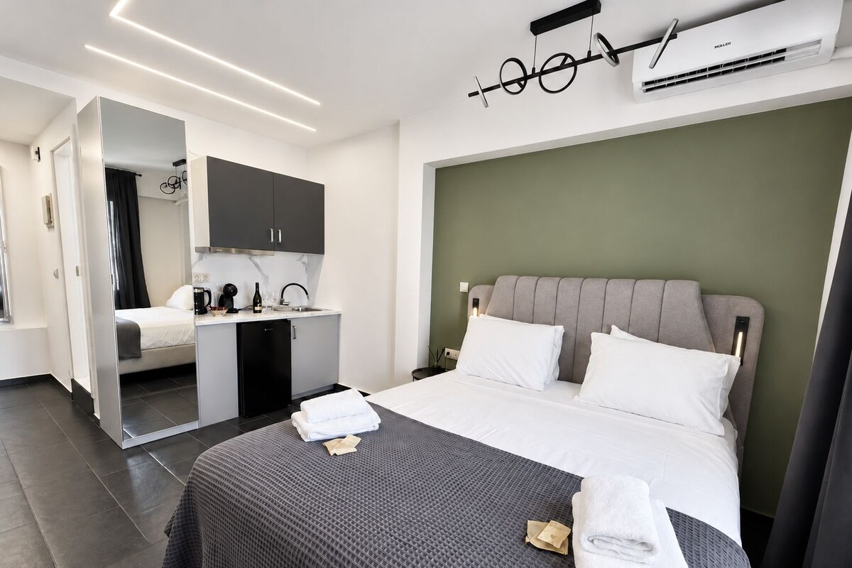 A modern hotel room with a bed, bedside table, and a built-in kitchen area.