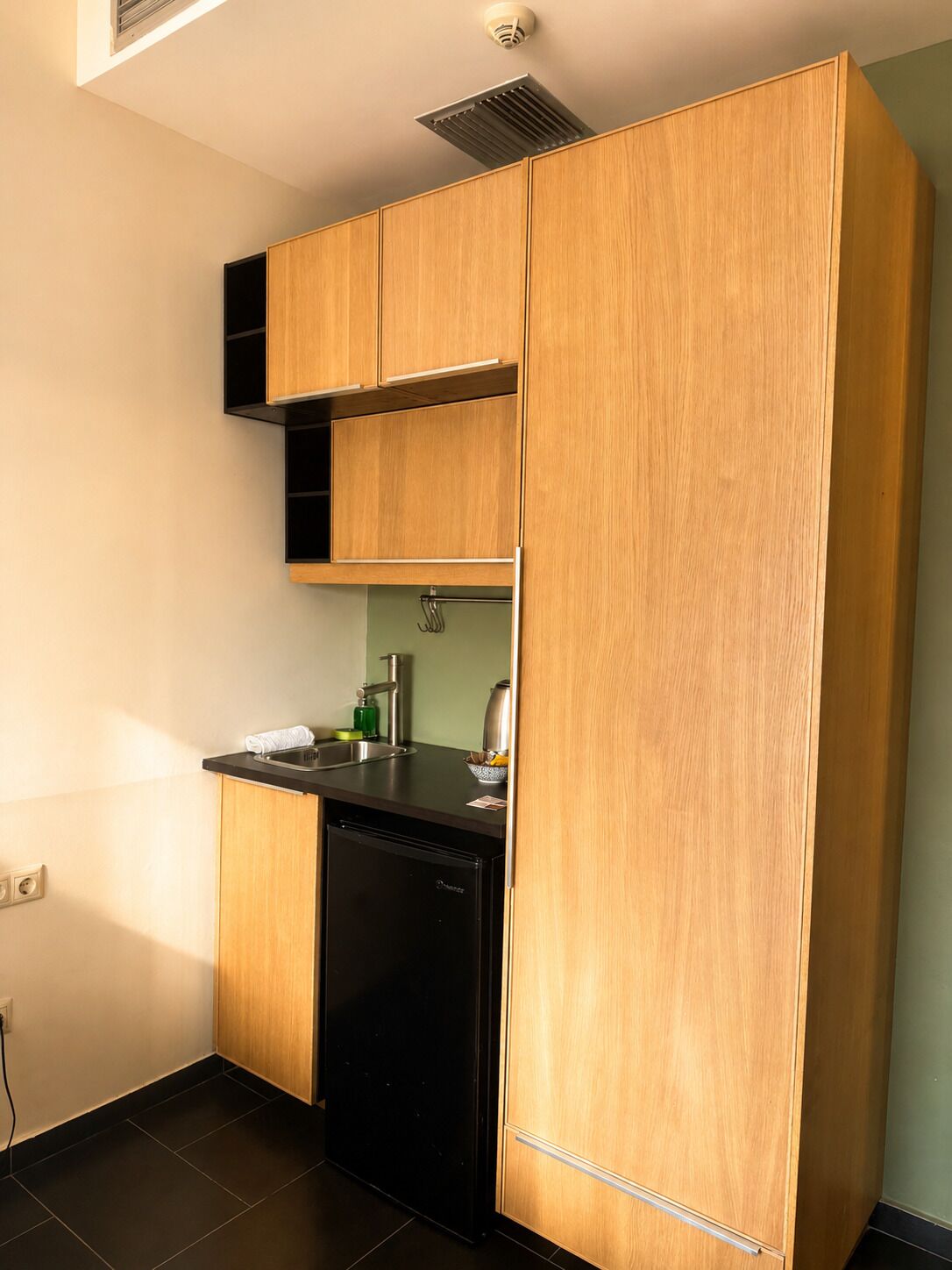 A compact kitchen with wooden cabinets, a black dishwasher, and a stainless steel sink.