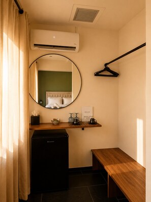 A compact hotel room with a bed, a small desk, a mirror, a heater, and a bench. - Elite Ermou Suites (Athens)