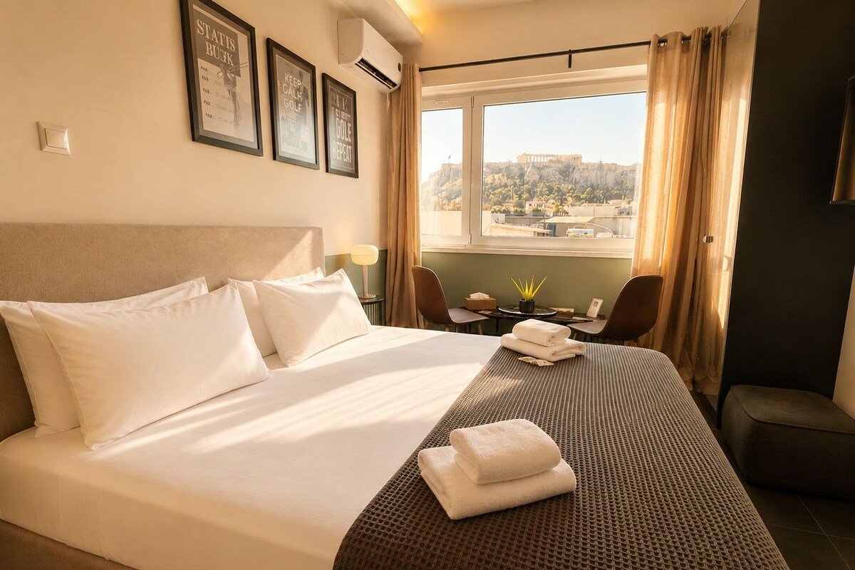 Quarto de hotel com uma cama grande, vista para a cidade e uma mesinha com uma planta.