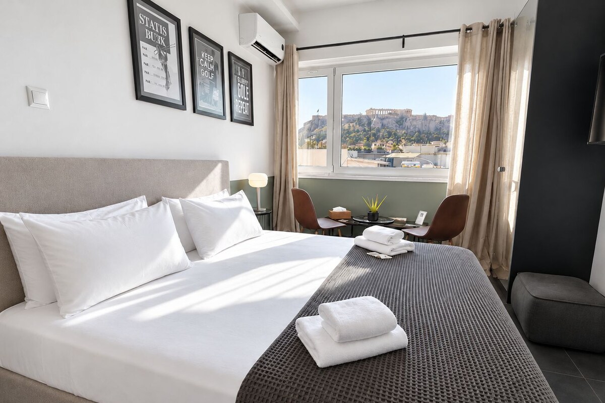 A hotel room with a bed, a desk, a chair, and a view of a historical building.
