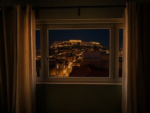 A window with a view of a historic cityscape at night, including a prominent hilltop structure. - Elite Ermou Suites (Athens)