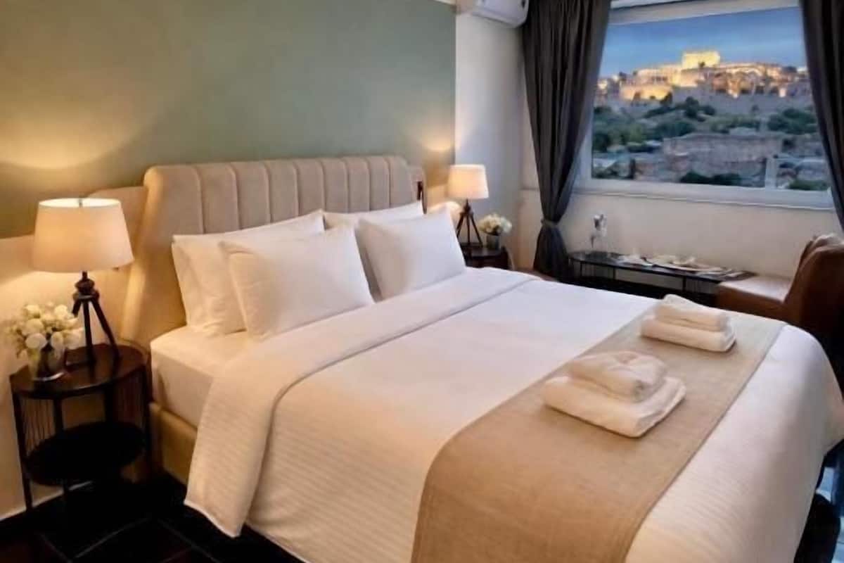 A hotel room with a bed, bedside tables, a window with a view, and a nightstand with a lamp.