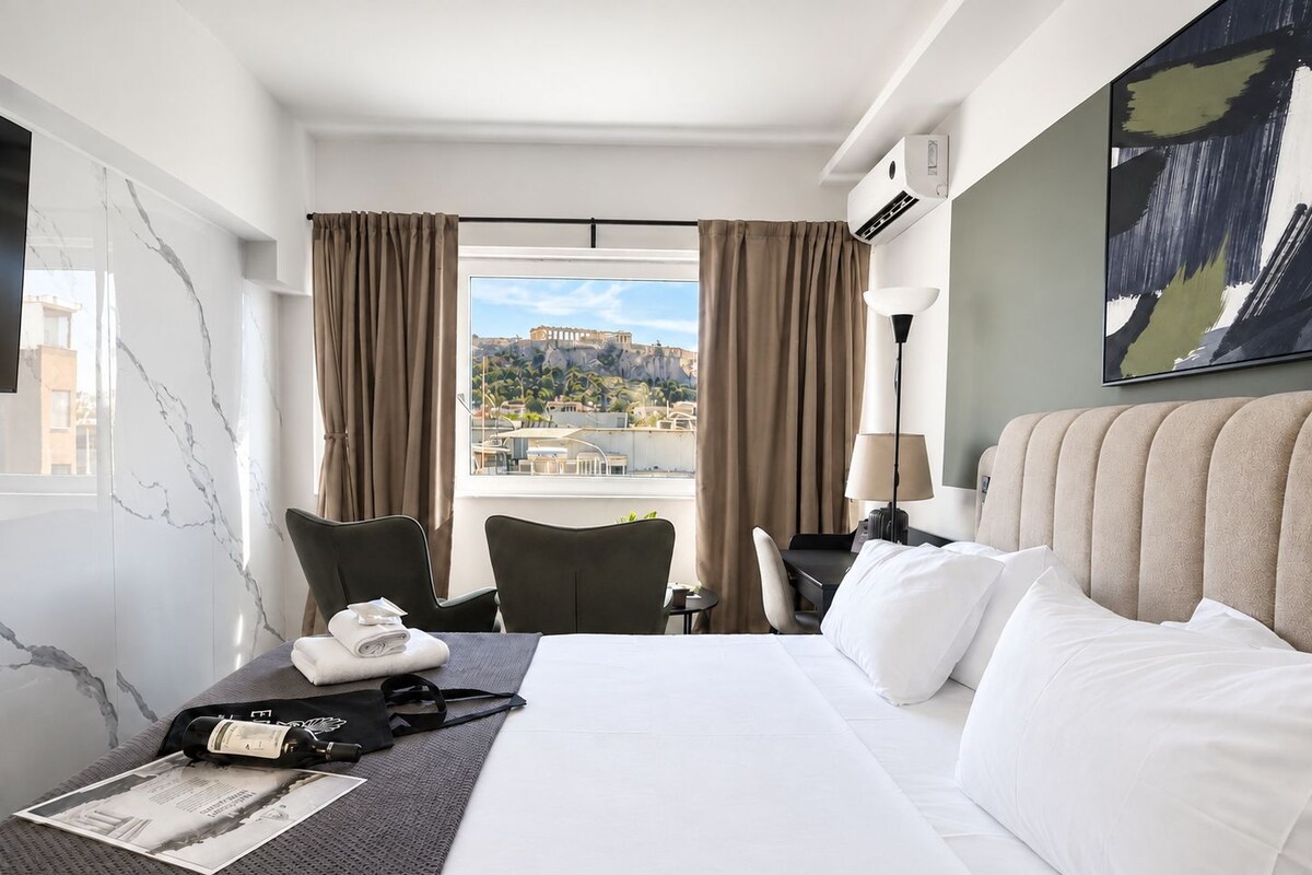 A hotel room with a bed, a desk, a chair, a window with curtains, and a view of a cityscape.