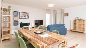 A modern living room with a wooden dining table, green chairs, a blue sofa, and a TV. - Premium Business Apartment (Vienna)