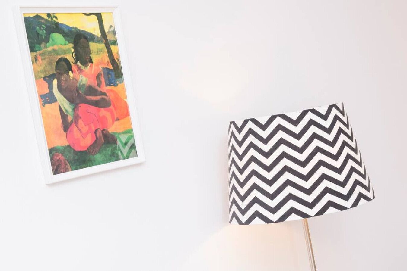 Een lijst met schilderij en een lamp met een zigzaagpatroon op een witte muur.