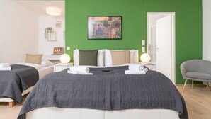 A hotel room with two beds, a green accent wall, a painting, and a chair. - Premium Business Apartment (Vienna)