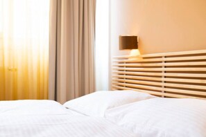 A hotel room with a bed, curtains, and a wall-mounted lamp.