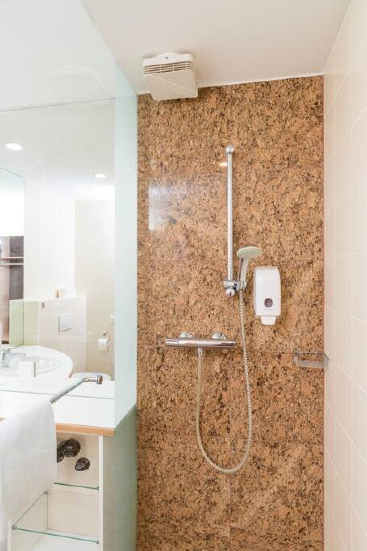 A modern bathroom with a granite shower wall, a handheld showerhead, and a built-in soap dispenser.