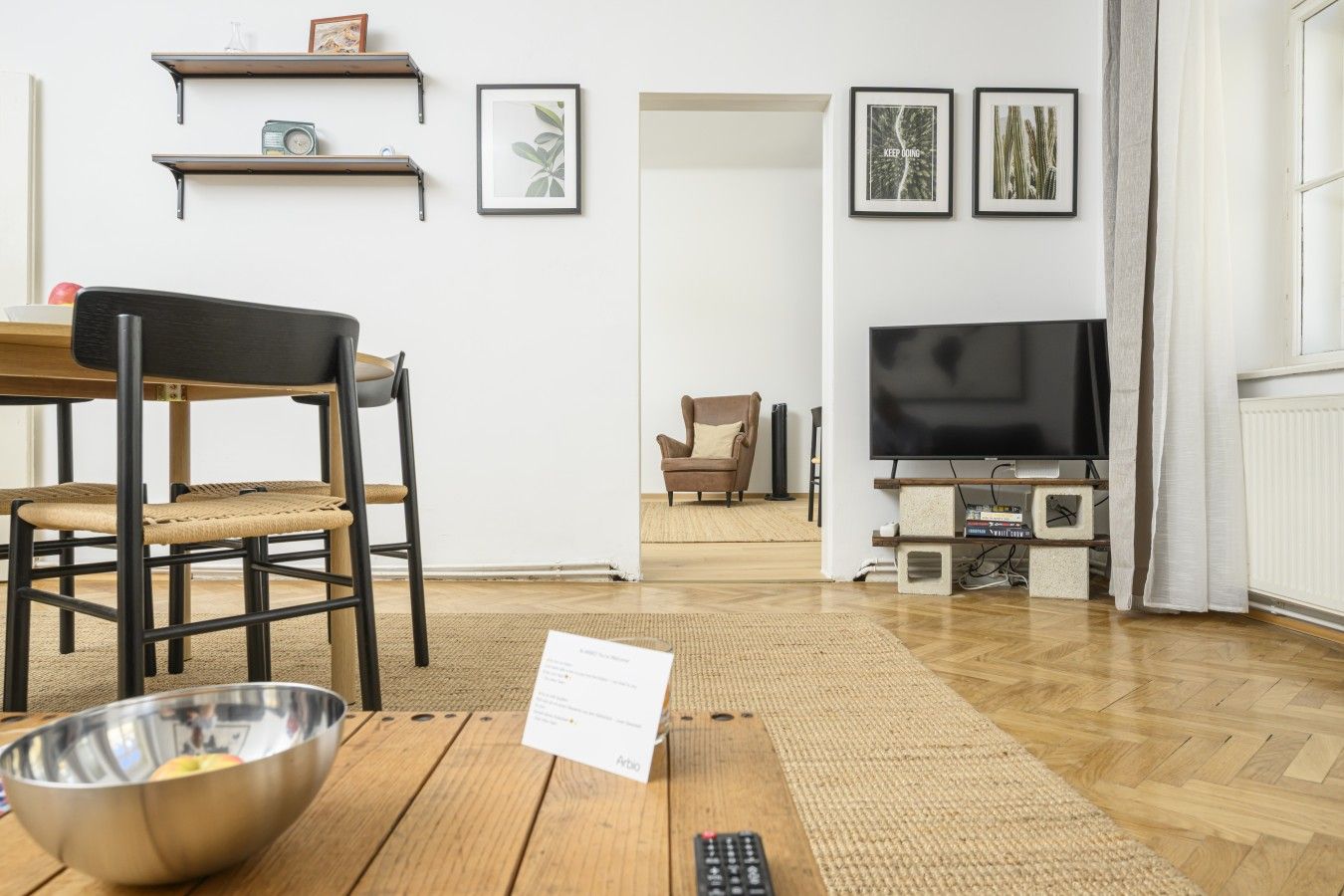 A living room with a wooden dining table, chairs, a TV, and framed pictures on the wall.