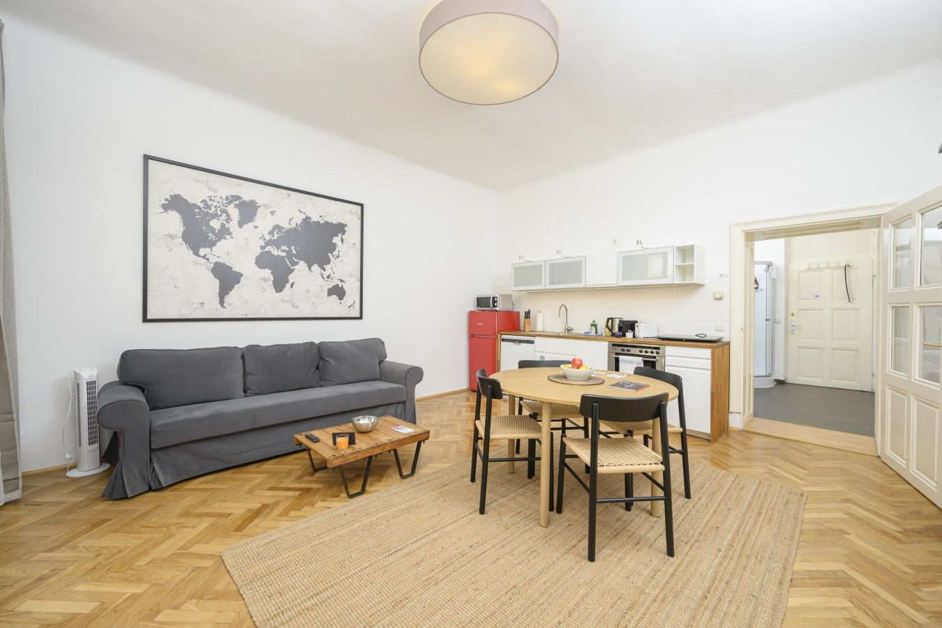 Ein gemütlicher Wohnraum mit grauem Sofa, einem runden Esstisch und einer Küchenzeile mit weißen Schränken.