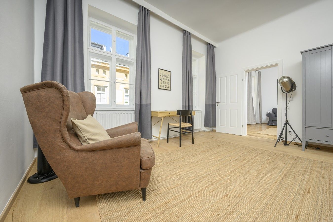 A room with a brown armchair, a small table, a tripod lamp, and a wardrobe.