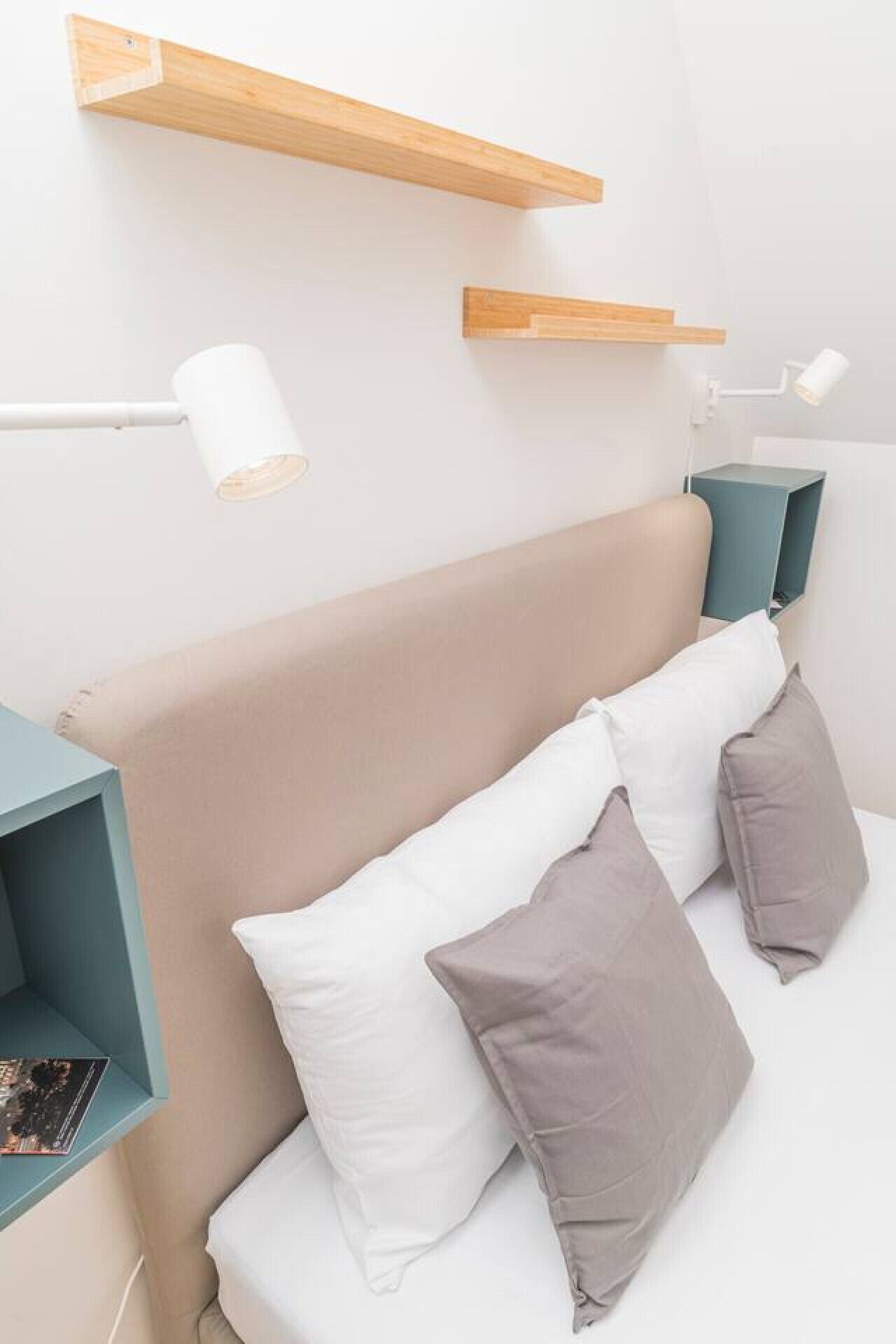 Un dormitorio con cama, almohadas, una mesita de noche y una lámpara de escritorio.