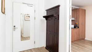A hallway with a white door, a dark wooden wardrobe, and a kitchen area with wooden cabinets and a countertop. - Apartment Favoriten top 1 (Vienna)