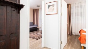 A hotel room with a dark wooden wardrobe, a framed picture on the wall, a grey sofa with a patterned rug, and a bed with an orange blanket. - Apartment Favoriten top 1 (Vienna)
