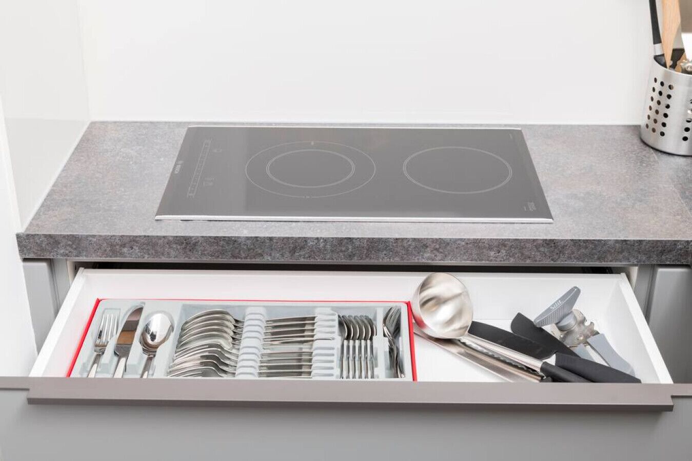 Une cuisine dotée d’une plaque de cuisson à induction intégrée et d’un tiroir contenant des ustensiles rangés de manière ordonnée.