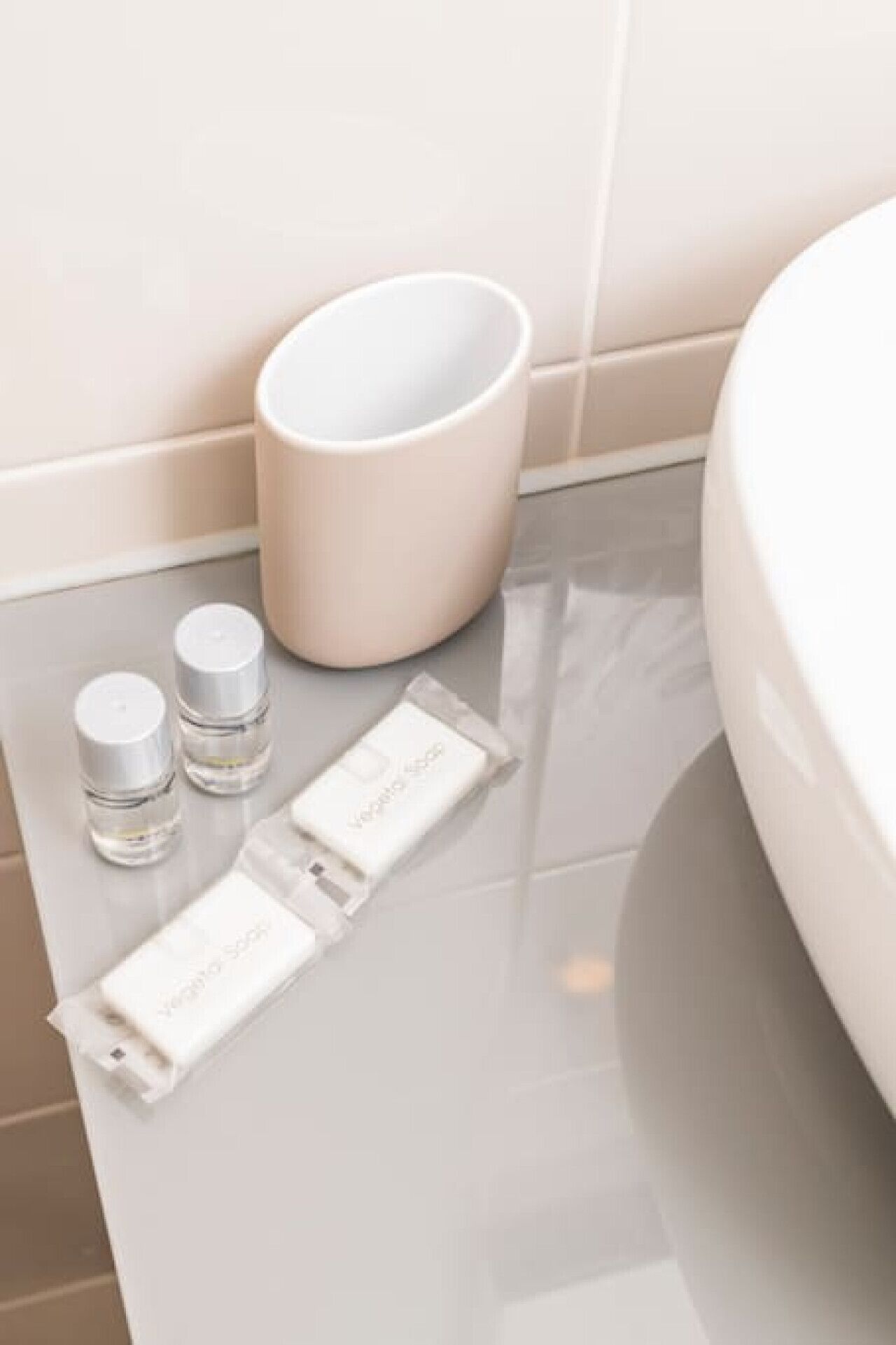 A bathroom with a white sink, a beige trash bin, and three toiletry bottles and a bar of soap on the counter.