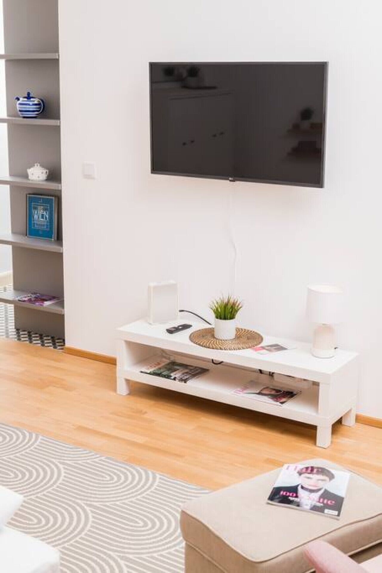 A modern living room with a flat-screen TV mounted on the wall, a white console table with decorative items, and a patterned rug on the floor.
