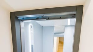 Een lift met een metalen frame en een glazen deur, die uitkomt op een betegelde vloer en een trap.