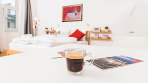 Een hotelkamer met een opgemaakt bed, een koffiemok op een tafel en een ingelijst foto aan de muur.