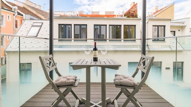 Een balkon met een tafel en twee stoelen, met uitzicht op een stadsbeeld met moderne gebouwen.