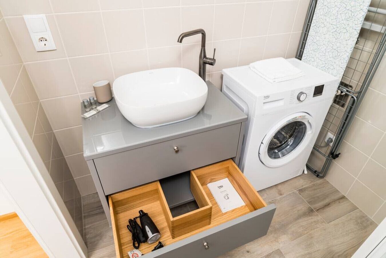 A modern bathroom with a sink, a washing machine, and a wooden drawer unit.