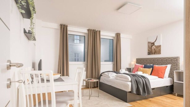 Una habitación de hotel moderna con cama, mesita de noche y una zona de comedor con mesa y sillas.