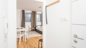 Habitación de hotel con piso de madera, cama con ropa blanca, escritorio con silla y ventana con cortinas.