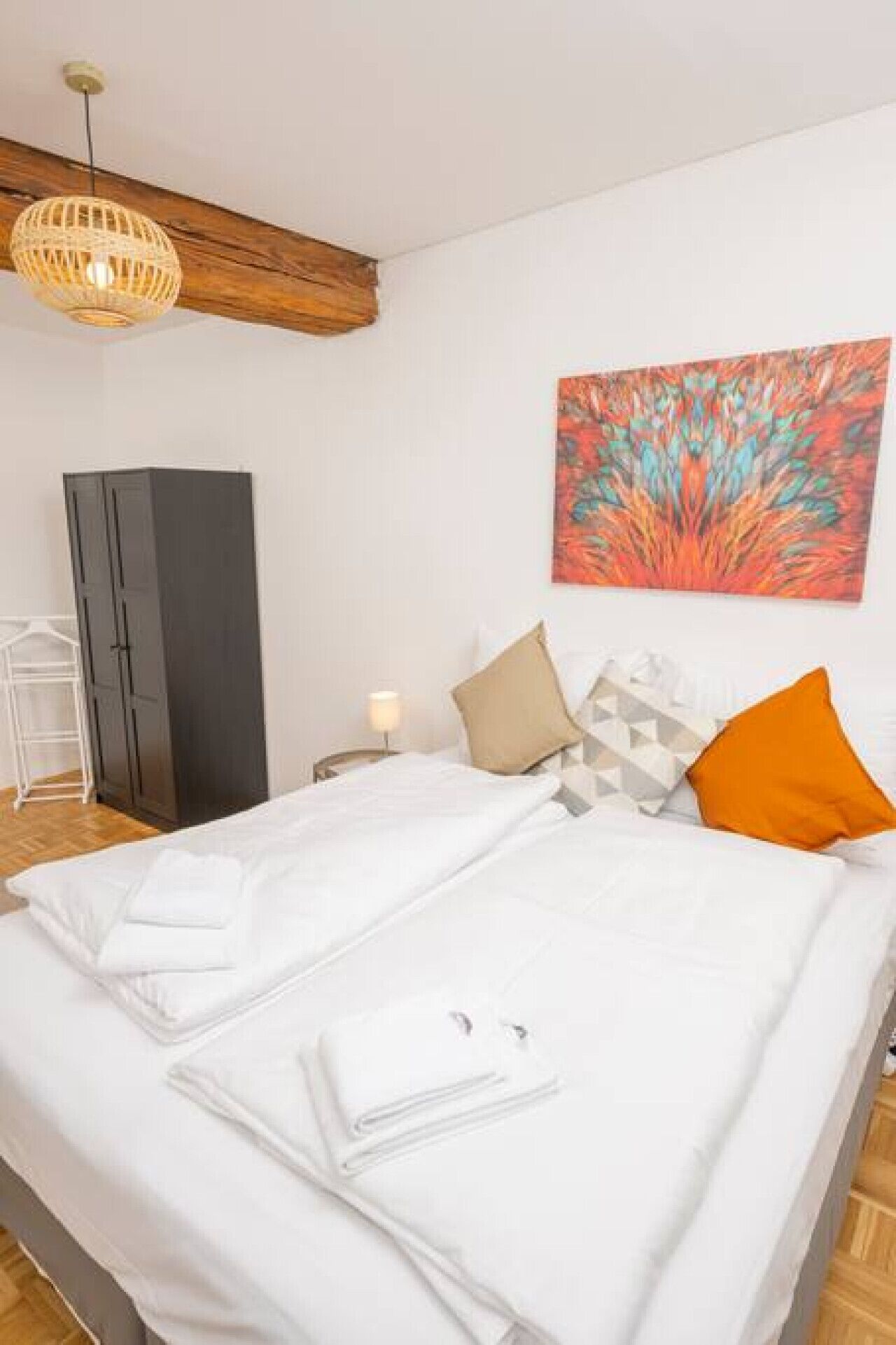 Ein ordentlich bezogenes Bett mit weißen Leinentüchern, ein Holz-Kopfteil, ein an der Wand hängendes abstraktes Gemälde und ein Nachttisch mit einer Lampe.