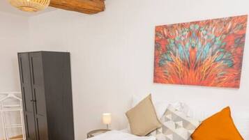 Ein ordentlich bezogenes Bett mit weißen Leinentüchern, ein Holz-Kopfteil, ein an der Wand hängendes abstraktes Gemälde und ein Nachttisch mit einer Lampe.