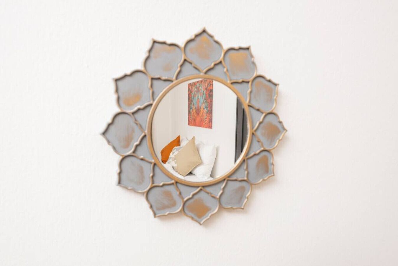 Un mirall fixat a la paret amb un marc metàl·lic decoratiu i un disseny geomàtric.