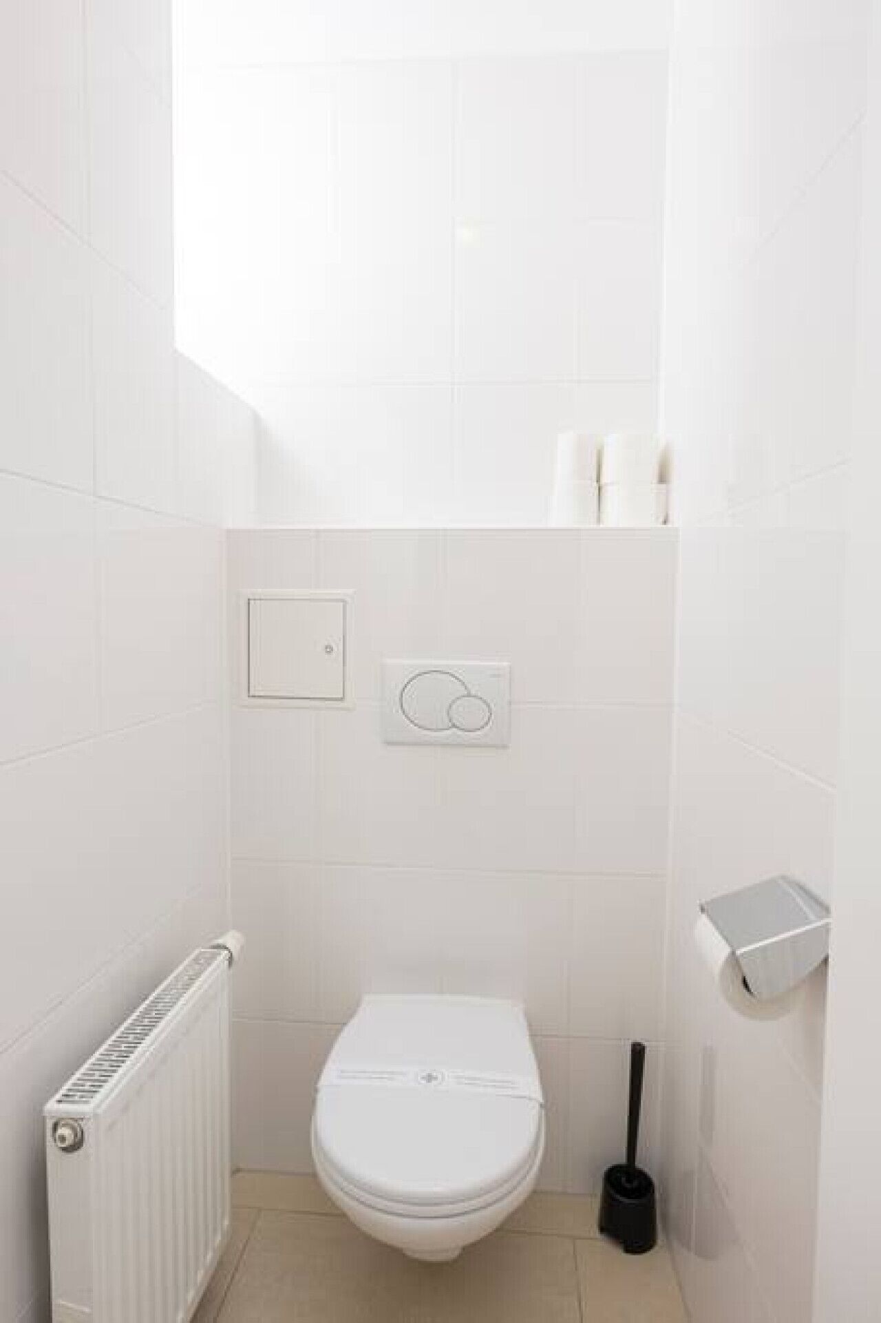 Un bagno piccolo e bianco con un water, un termosifone e un portasciugamani per carta igienica.