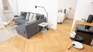 Moderni olohuone, jossa on harmaa sohva, pieni sivupöytä ja kahvinkeitin.
