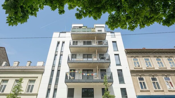 Un immeuble à plusieurs étages doté de balcons, un ciel dégagé et des arbres.
