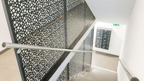 Un escalier agrémenté d’une cloison en métal perforé et d’un panneau de commande fixé au mur.
