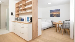 Une pièce de taille modeste comprenant un lit, un petit bureau, une chaise, un coin cuisine équipé d’un four à micro-ondes et une bibliothèque.