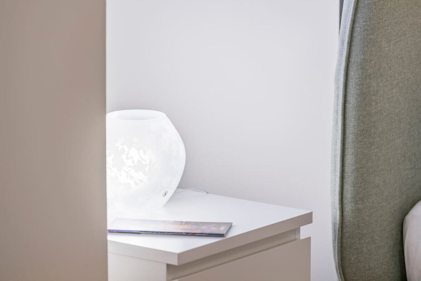 Ein weißer Nachttisch mit einer Lampe und einer Zeitschrift.