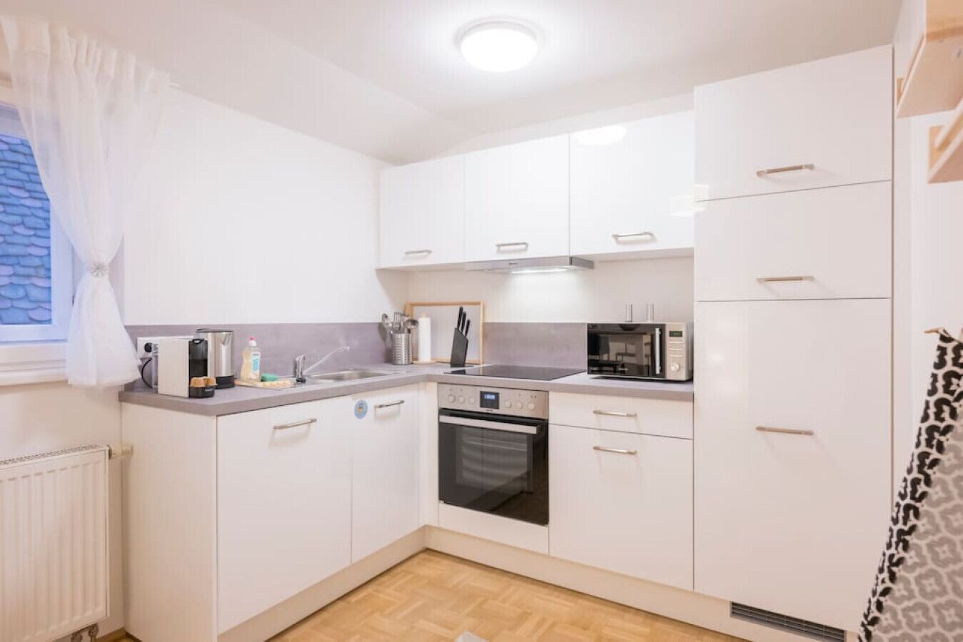 A compact kitchen with white cabinets, a built-in oven, a microwave, and a coffee maker.
