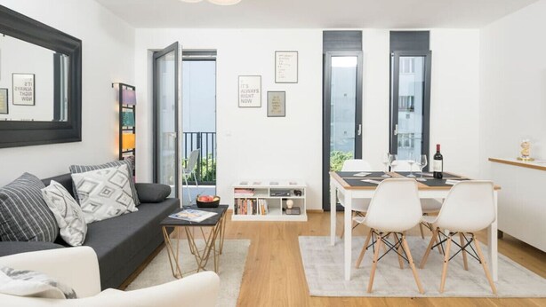 A modern living room with a sofa, a dining table with chairs, and a bookshelf. - Ottakring Balcony Suite (Vienna)