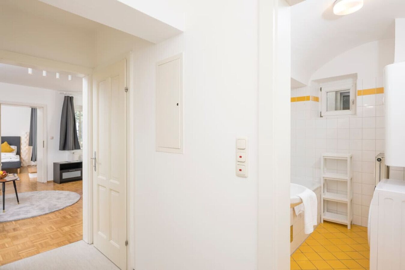 A hotel room with a wooden floor, a bed, a TV, and a bathroom with a yellow floor.