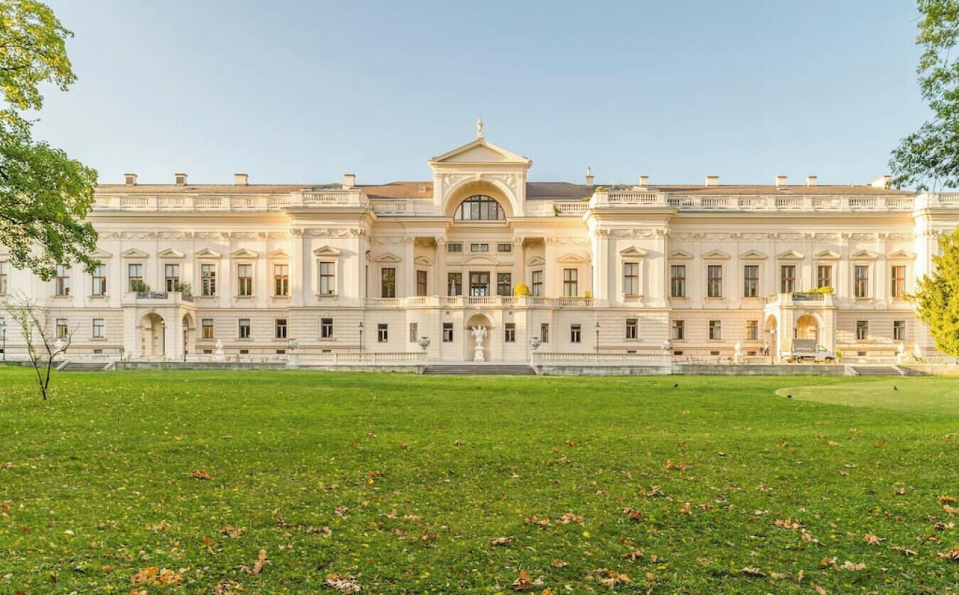 Un edificio grande de estilo clásico, con arquitectura simétrica, una cúpula central y un amplio césped delantero.