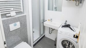 A compact bathroom with a toilet, a shower, a sink, and a washing machine. - Best of Hernals Top 24 (Vienna)